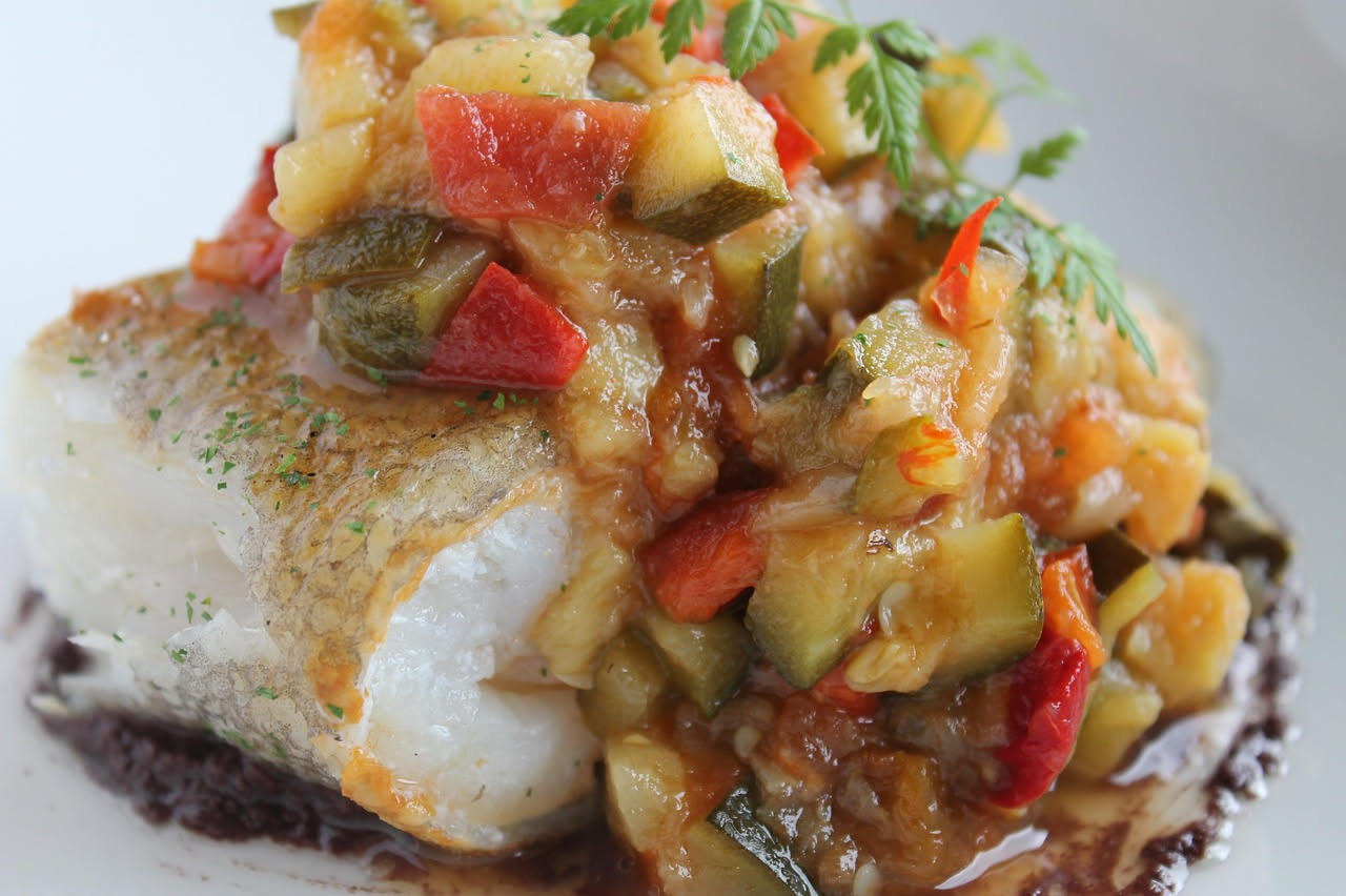 Stoccafisso cotto in umido in una pentola di coccio, circondato da pomodori rossi, olive nere e aglio, con il sugo che copre il pesce in pezzi