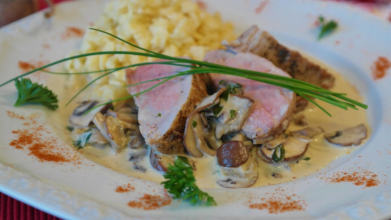 Tagliatelle dorate condite con funghi misti rossicci e bianchi, burro e prezzemolo fresco, impiattate in un piatto bianco fondo con formaggio grattugiato a lato