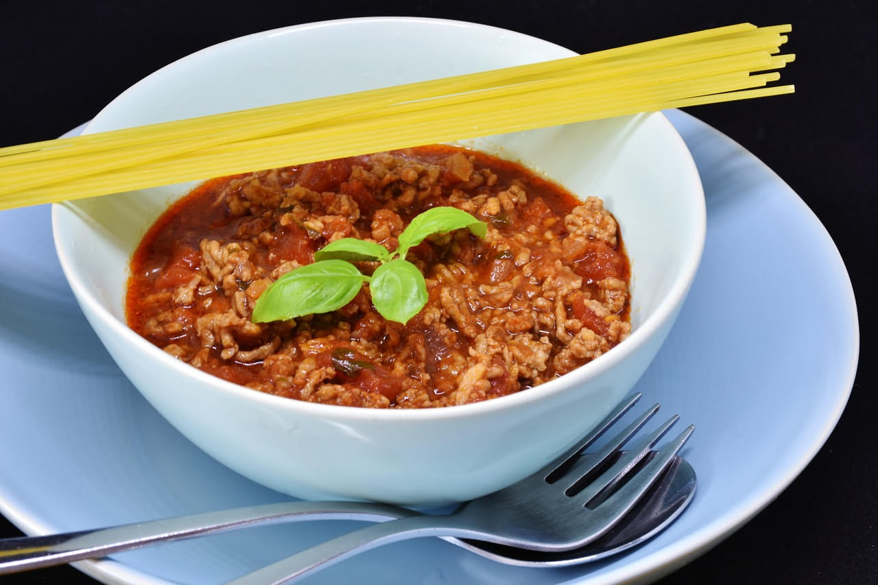 Piatto di tagliatelle al ragù con pasta gialla arrotolata, sugo marrone rossiccio e ricotta bianca grattugiata sopra, servito su piatto bianco