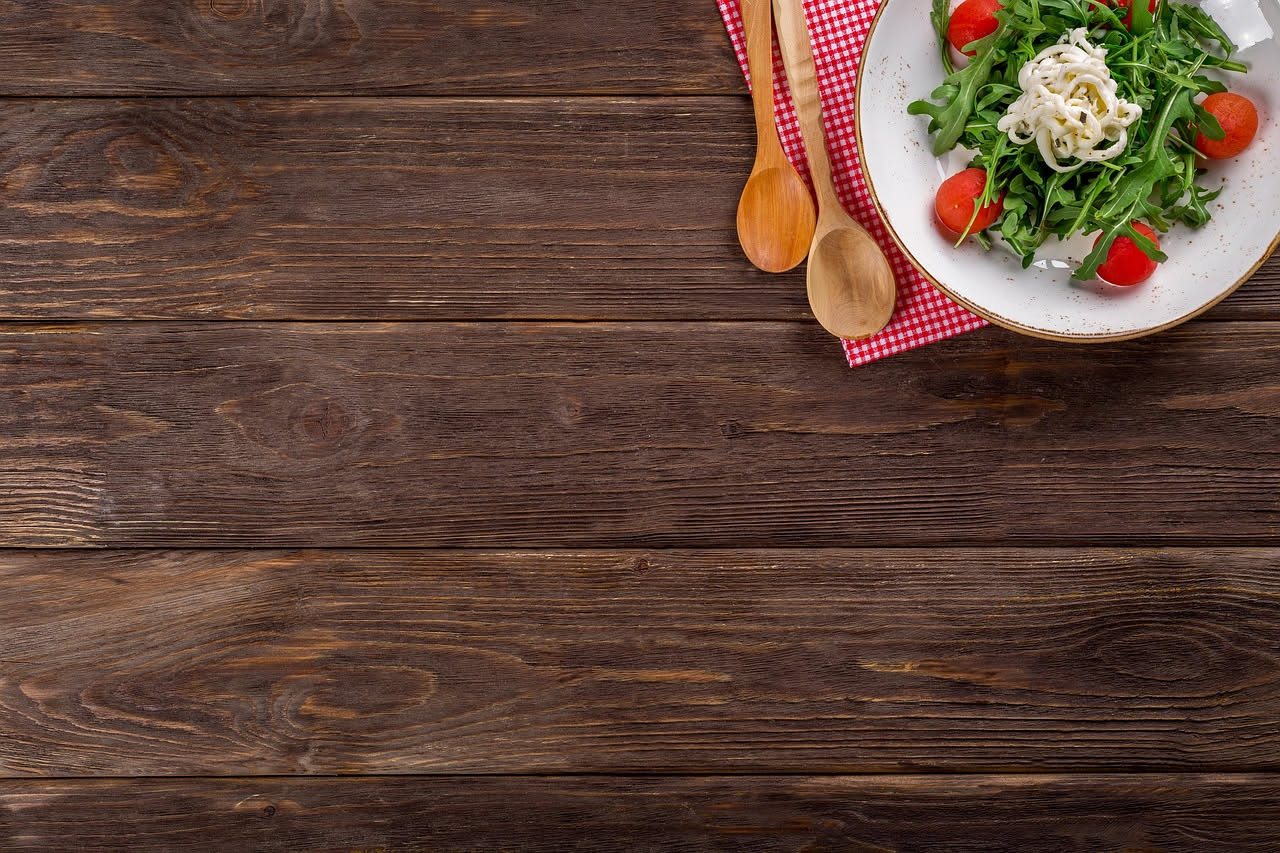 Un piatto di ceramica bianca con tagliatelle gialle coperte di rucola verde brillante, panna bianca e scaglie di parmigiano dorato, olio d'oliva lucido in superficie