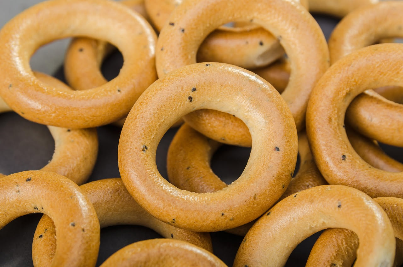 Taralli all'olio disposti su un piatto bianco, tondi e leggermente dorati, con superficie irregolare e croccante, sfondo grigio neutro