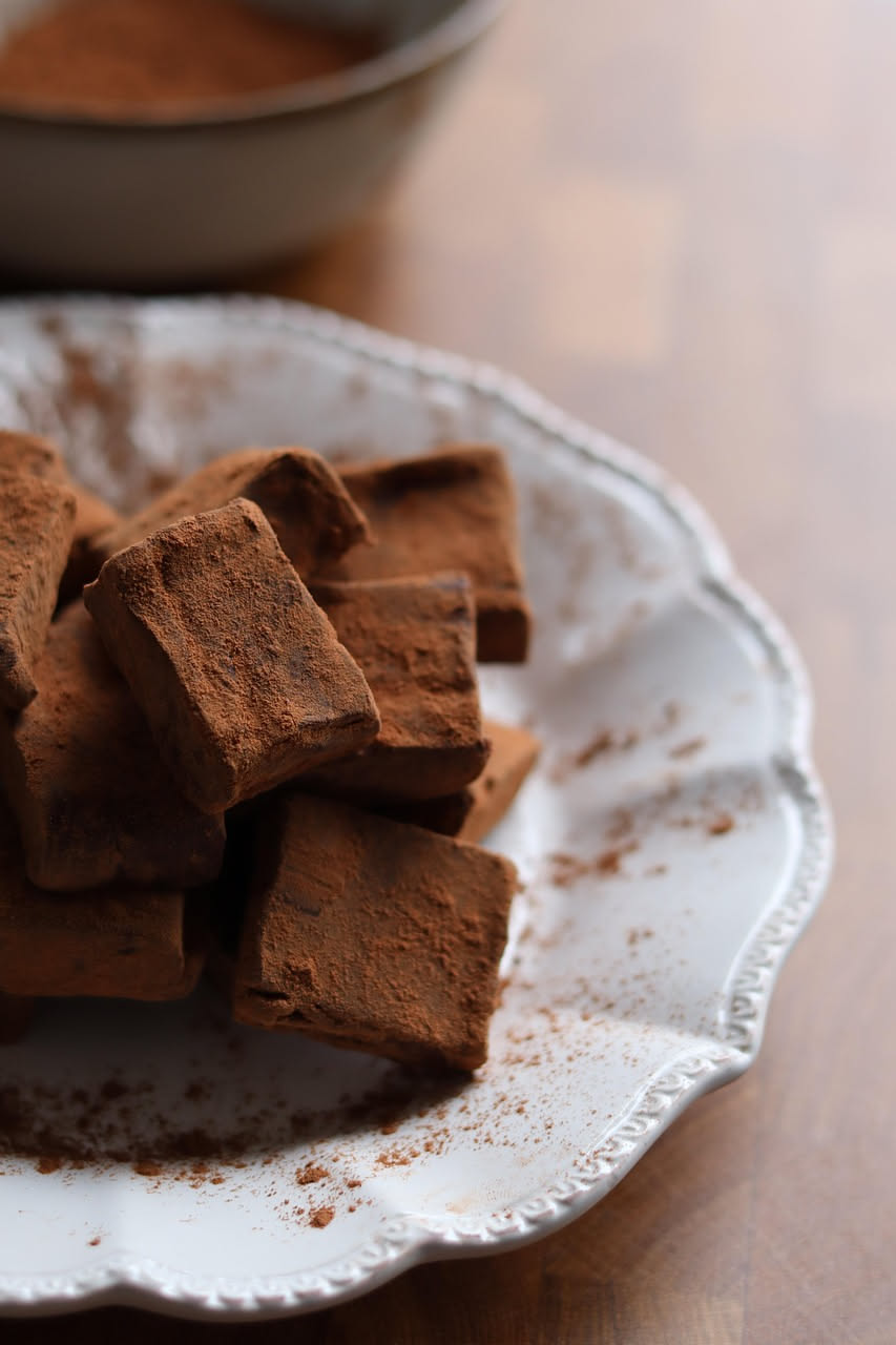 Dieci tartufi tondi ricoperti di cacao in polvere marrone scuro, disposti su piattino bianco, con superficie leggermente screpolata e rugosa, luce naturale da sinistra