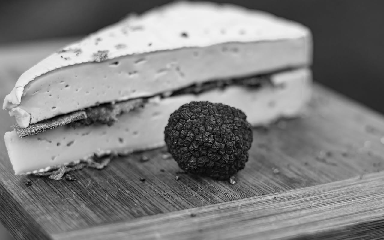 Tartufi neri interi e uno affettato sottile su tagliere di marmo bianco, accanto a un coltello per affettare e una grattugia piccola, con foglie di prezzemolo fresco