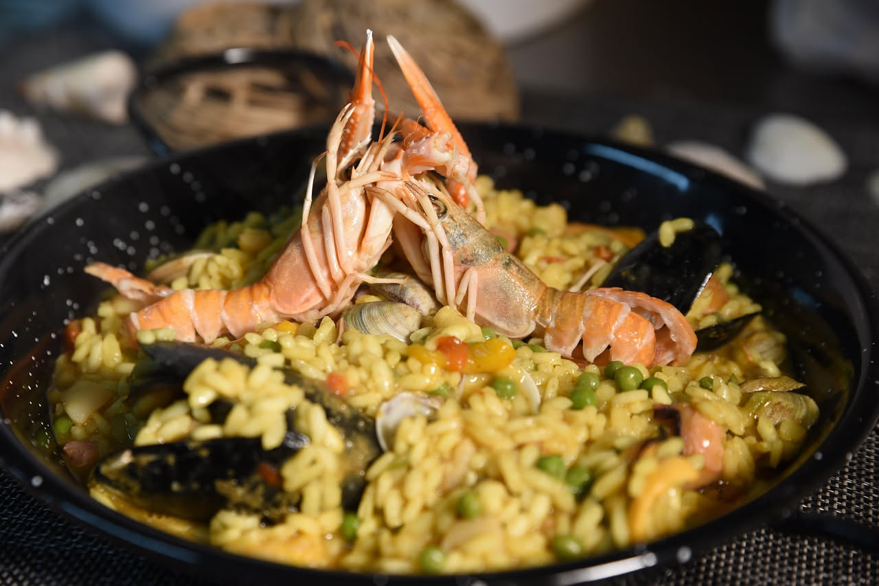Tiella di orzo e cozze in ciotola bianca: chicchi di orzo morbidi color beige mescolati a cozze aperte nere e brillanti, condite con olio verde oliva, prezzemolo fresco e una spremuta di limone visibi