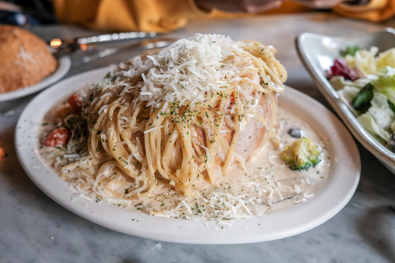 Timballo di pasta appena sfornato, dorato in superficie con crosta croccante, tagliato a fette che mostrano l'interno cremoso con ragù e pasta visibili, servito in un piatto bianco