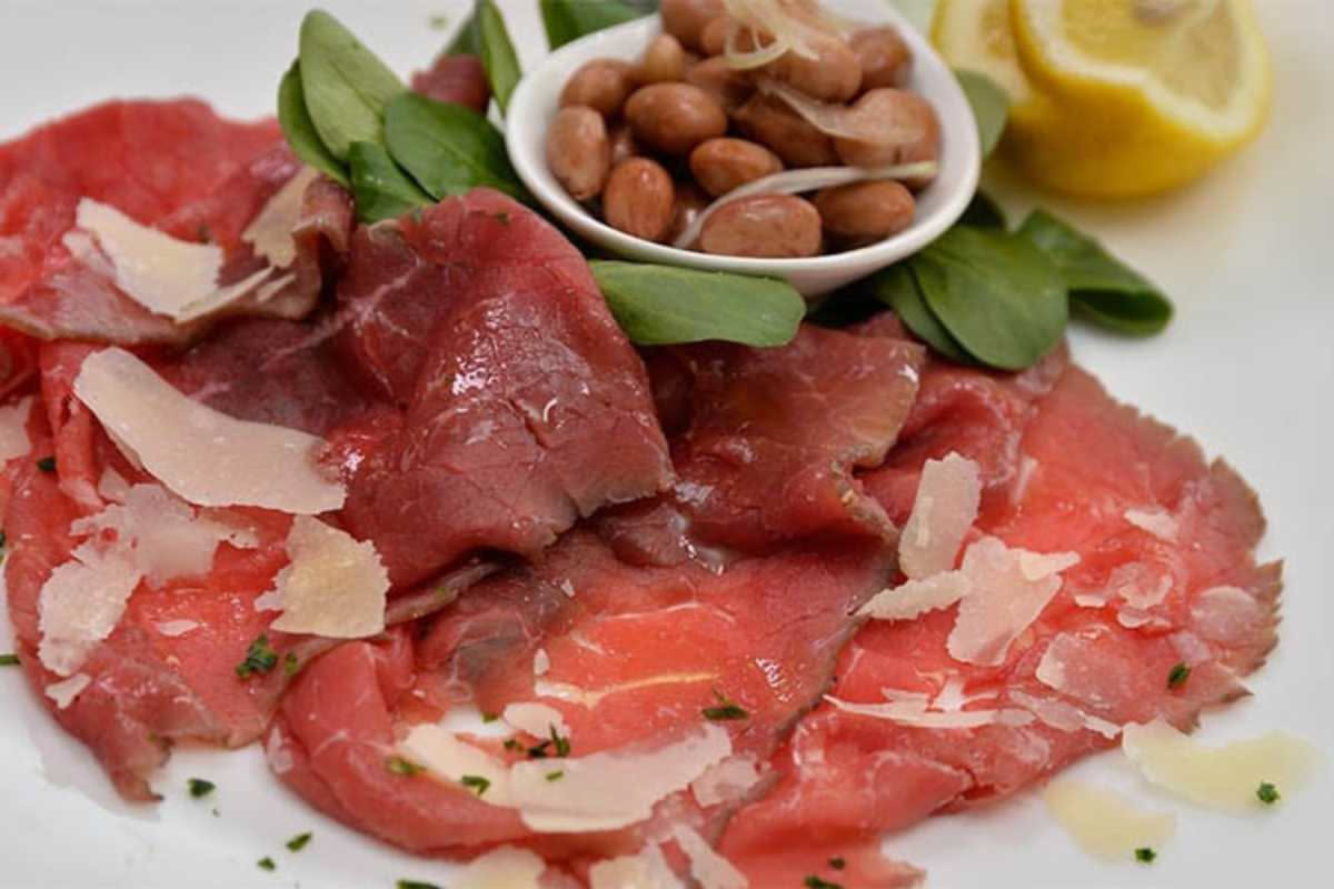 Ciotola bianca con tonno sott'olio sminuzzato, fagioli bianchi e rossi, cipolla rossa affettata e olio d'oliva fresco, posata su tavolo di legno naturale con limone intero