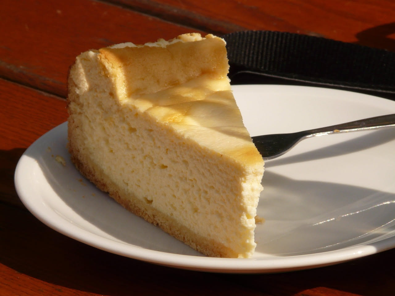 Torta al formaggio salato affettata, con base dorata e croccante, ripieno cremoso bianco e giallo, guarnita con erba cipollina e pepe nero, servita su piatto bianco
