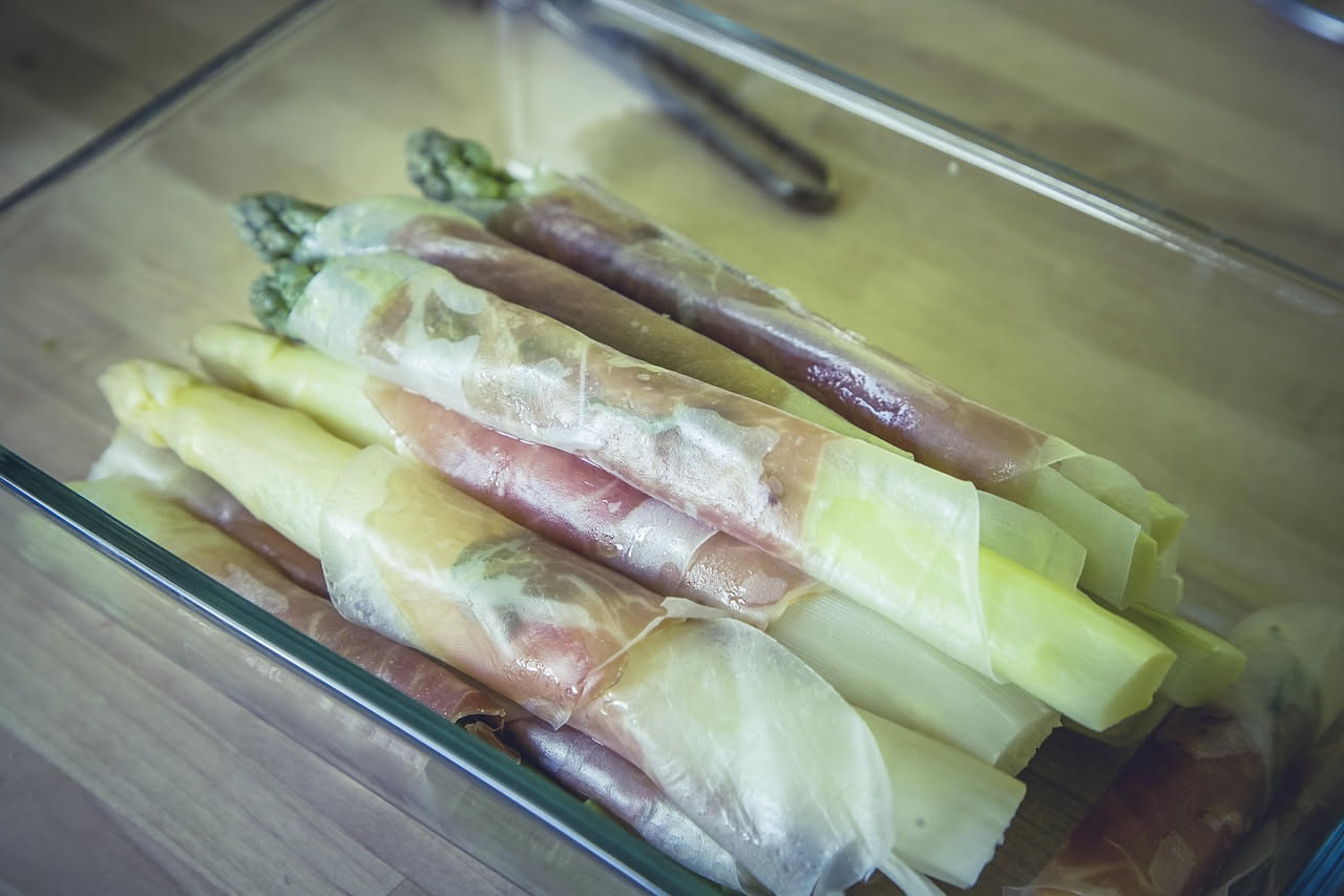 Torta d'asparagi fredda affettata in uno piatto bianco, con fette dorate e verdi, asparagi interi posizionati sulla superficie, condimento di parmigiano grattugiato, fondo di marmo bianco con foglie d