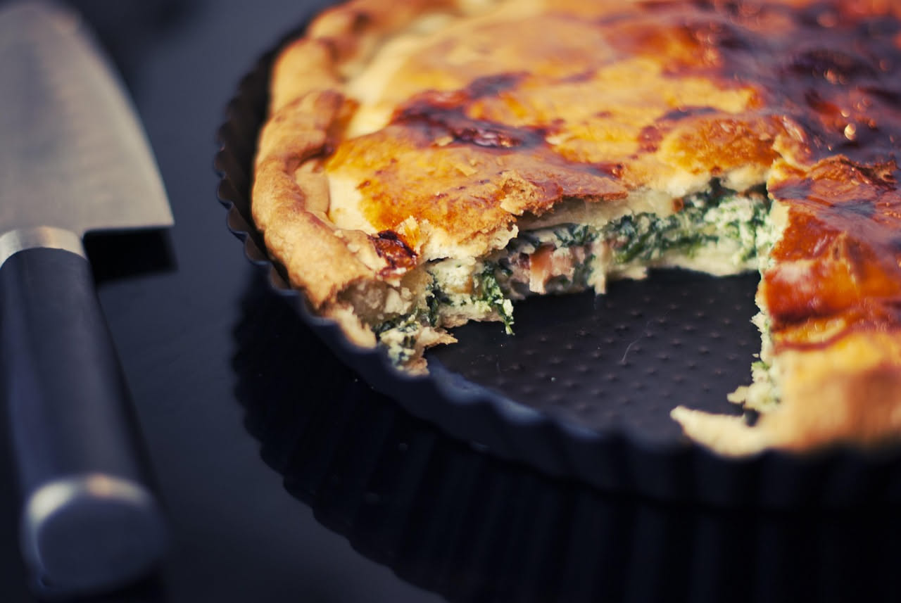 Fetta di torta di verdure dorata, ancora calda, con visibili zucchine, carote e spinaci all'interno, su un piatto bianco