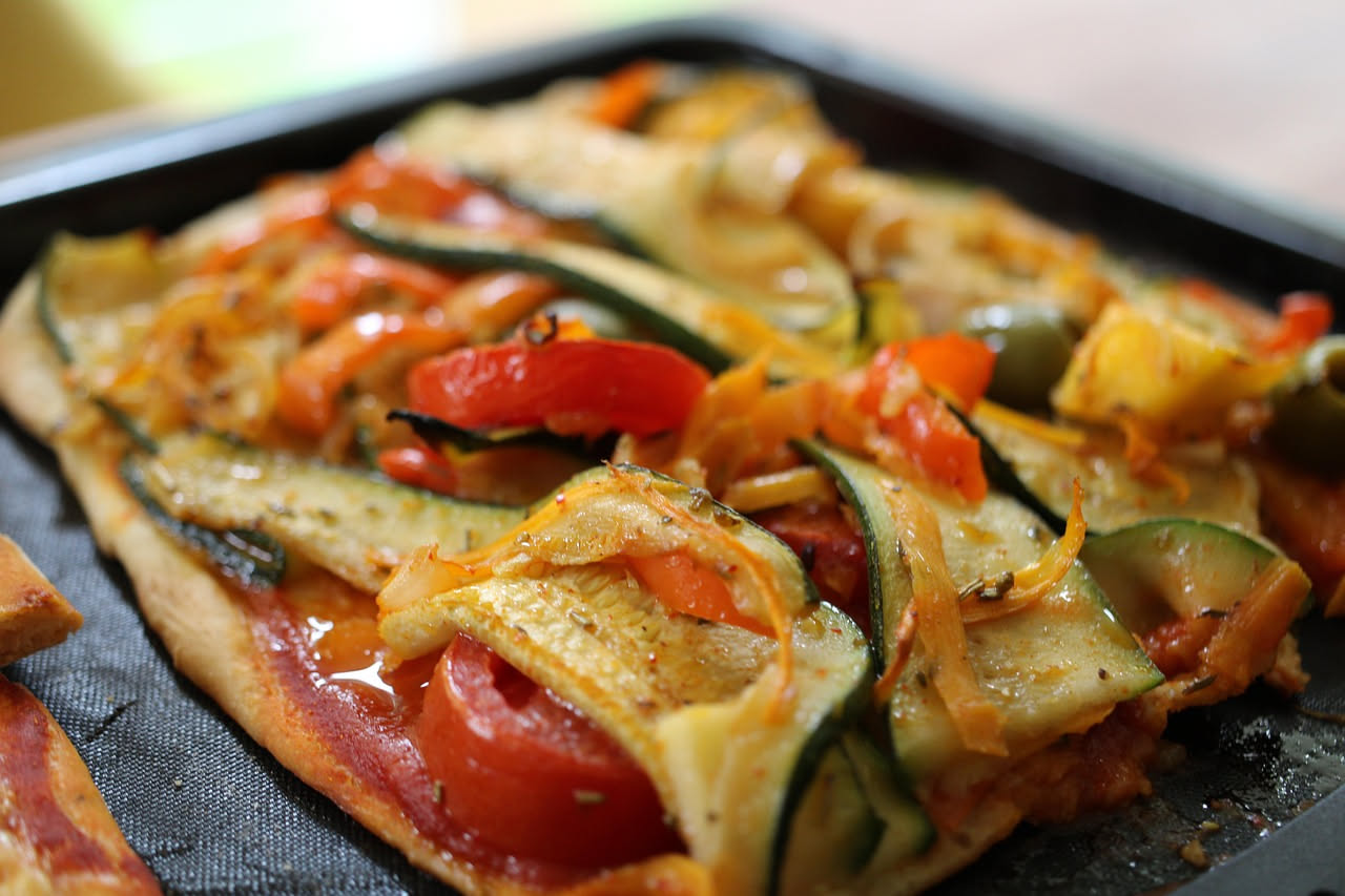 Torta salata con verdure appena sfornata, con zucchine gialle, melanzane e pomodori visibili sulla superficie dorata, in una teglia rotonda di alluminio, fondo chiaro