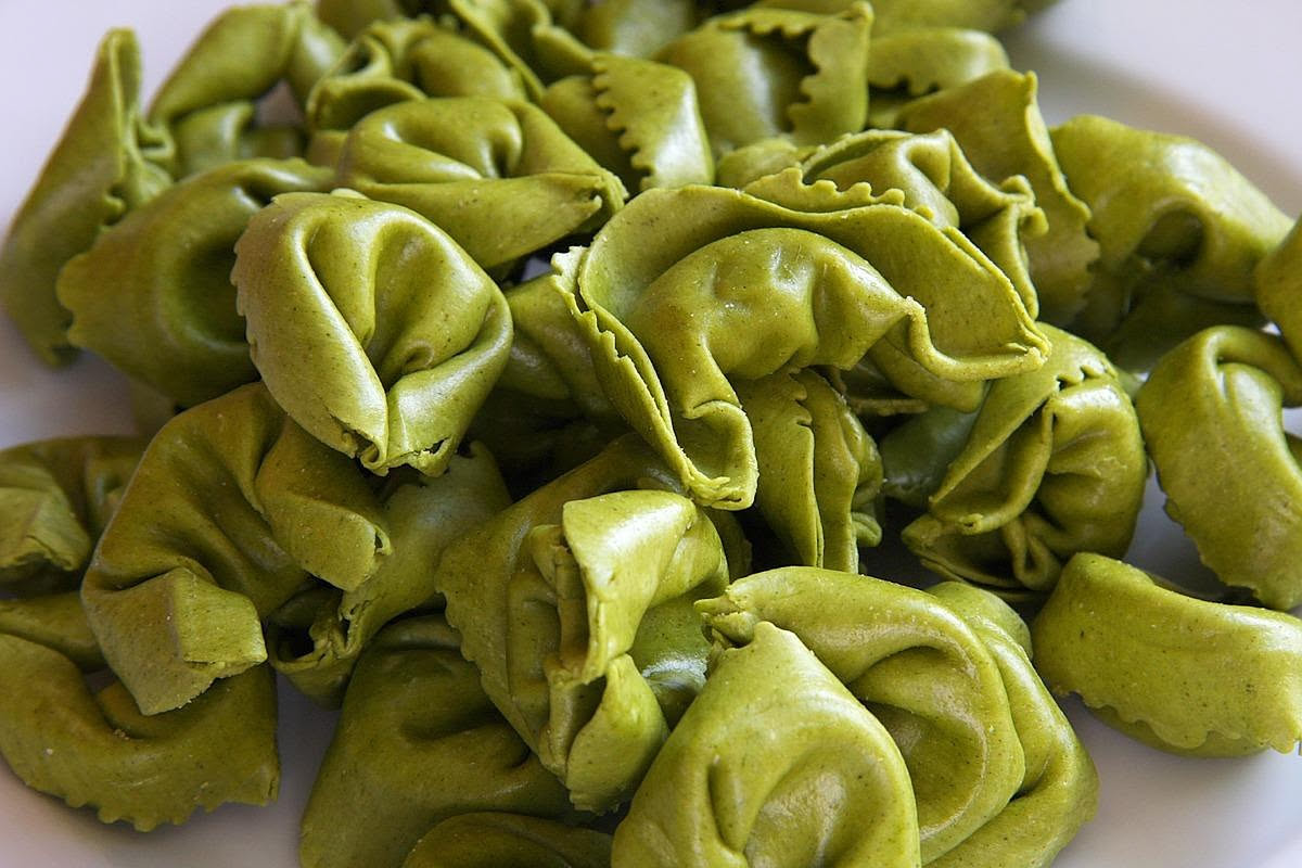 Tortelli di ricotta e spinaci ripieni disposti su un tavolo di legno infarinato, con sfoglia gialla e ripieno verde visibile da uno spaccato, accanto a una ciotola di ricotta bianca