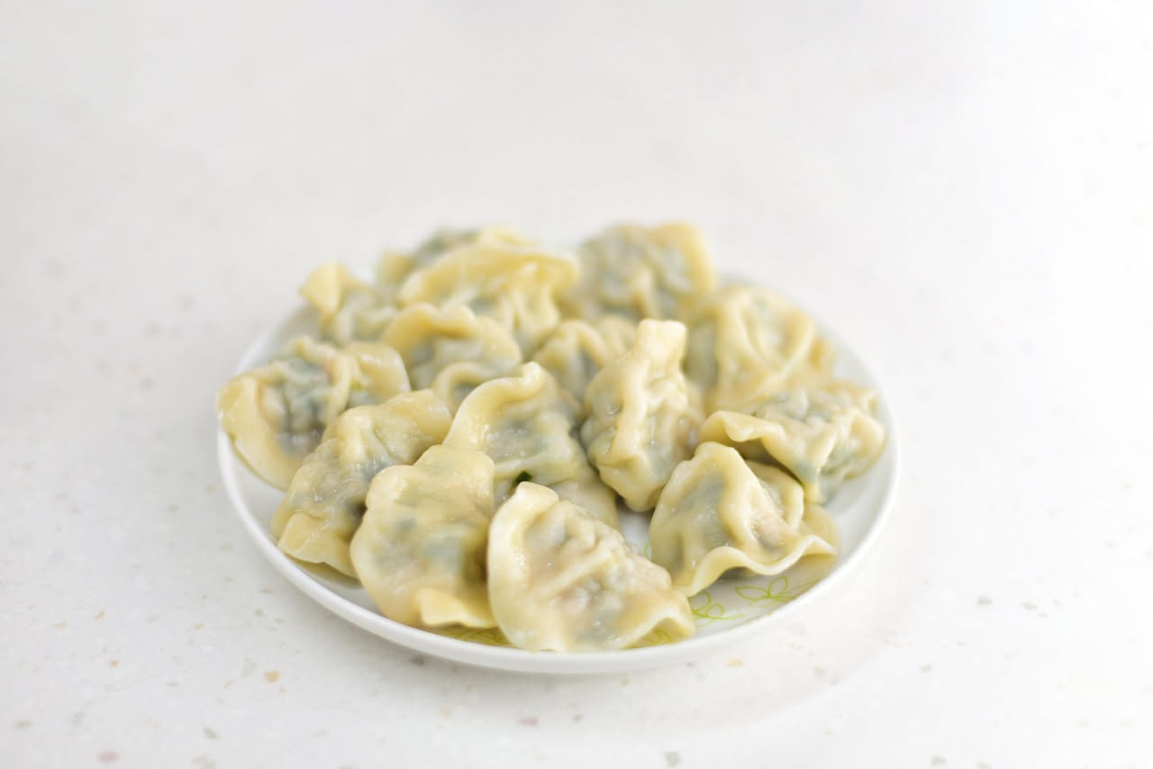 Tortelli di verdura quadrati di sfoglia gialla, disposti nel piatto bianco con burro sciolto, salvia verde e grana grattugiato visibile. Ripieno verde che esce leggermente dal bordo.