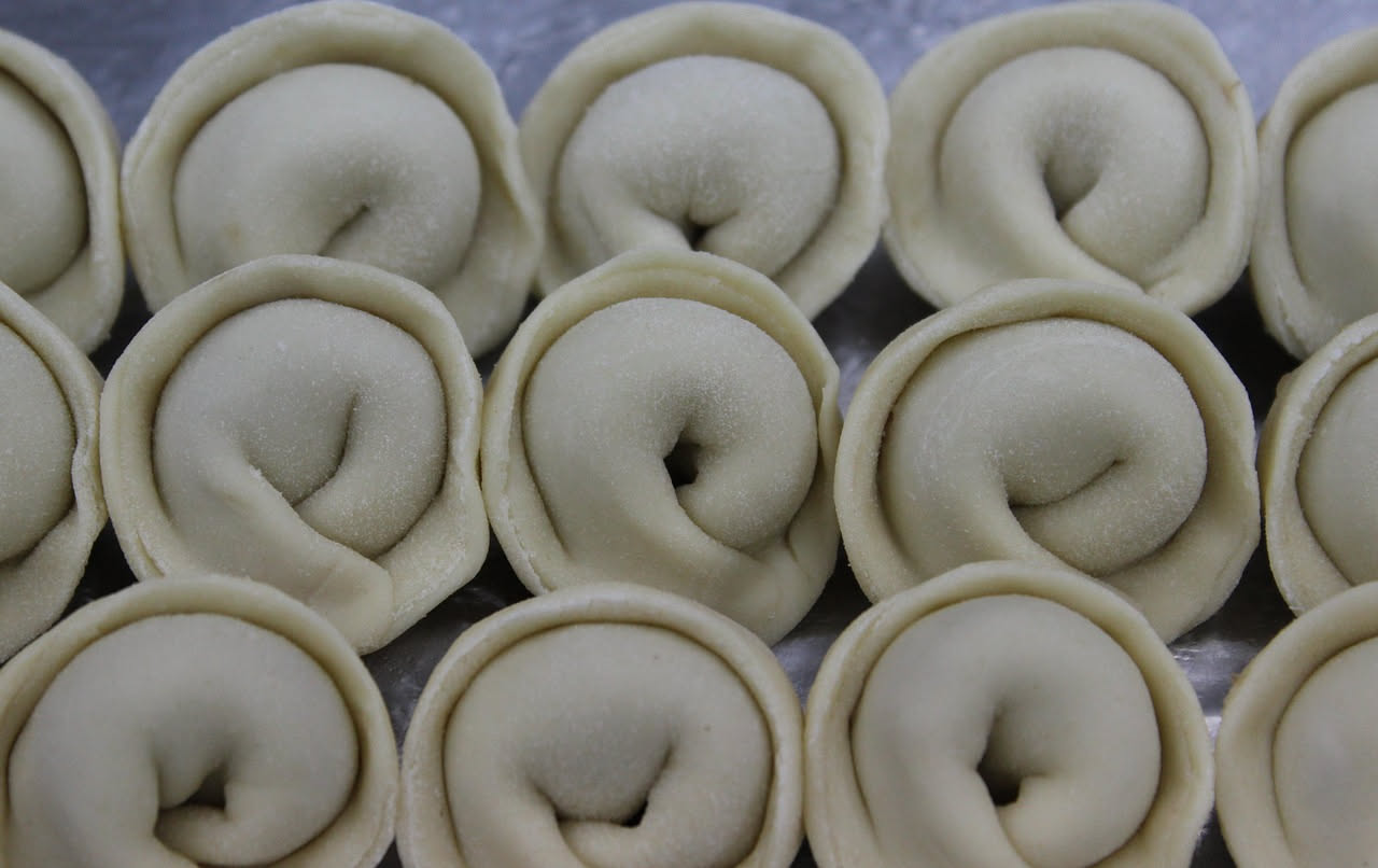 Tortellini di carne cotti in brodo di carne fumante, serviti in ciotola di porcellana bianca con fili di Parmigiano grattugiato e prezzemolo fresco.