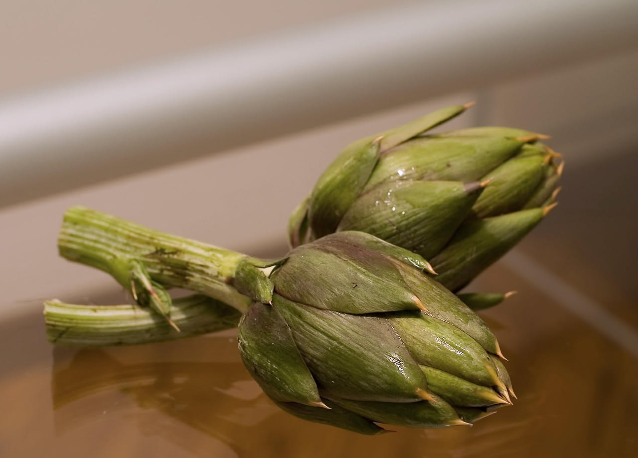 Tortino di carciofi tagliato in fette su un piatto bianco, con carciofi verdi e cremoso ripieno visibile al centro, servito con limone a fette