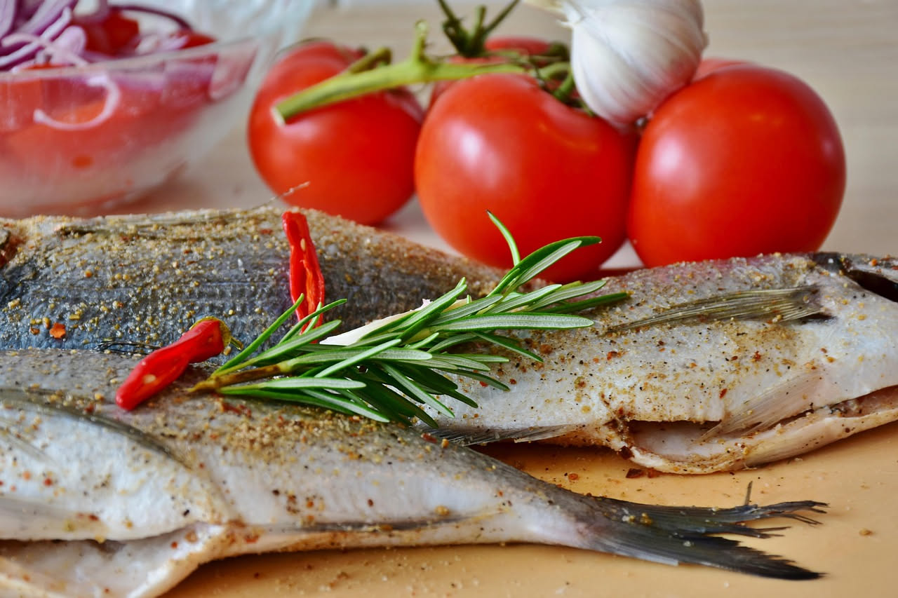 Triglie intere cotte in umido con sugo rosso di pomodoro, olive nere e capperi, servite in un piatto bianco fondo su tavolo di legno