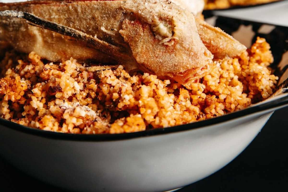 Piatto di triglie dorate fritte coperte di cipolla bianca caramellata e aceto, con basilico fresco, su fondo bianco