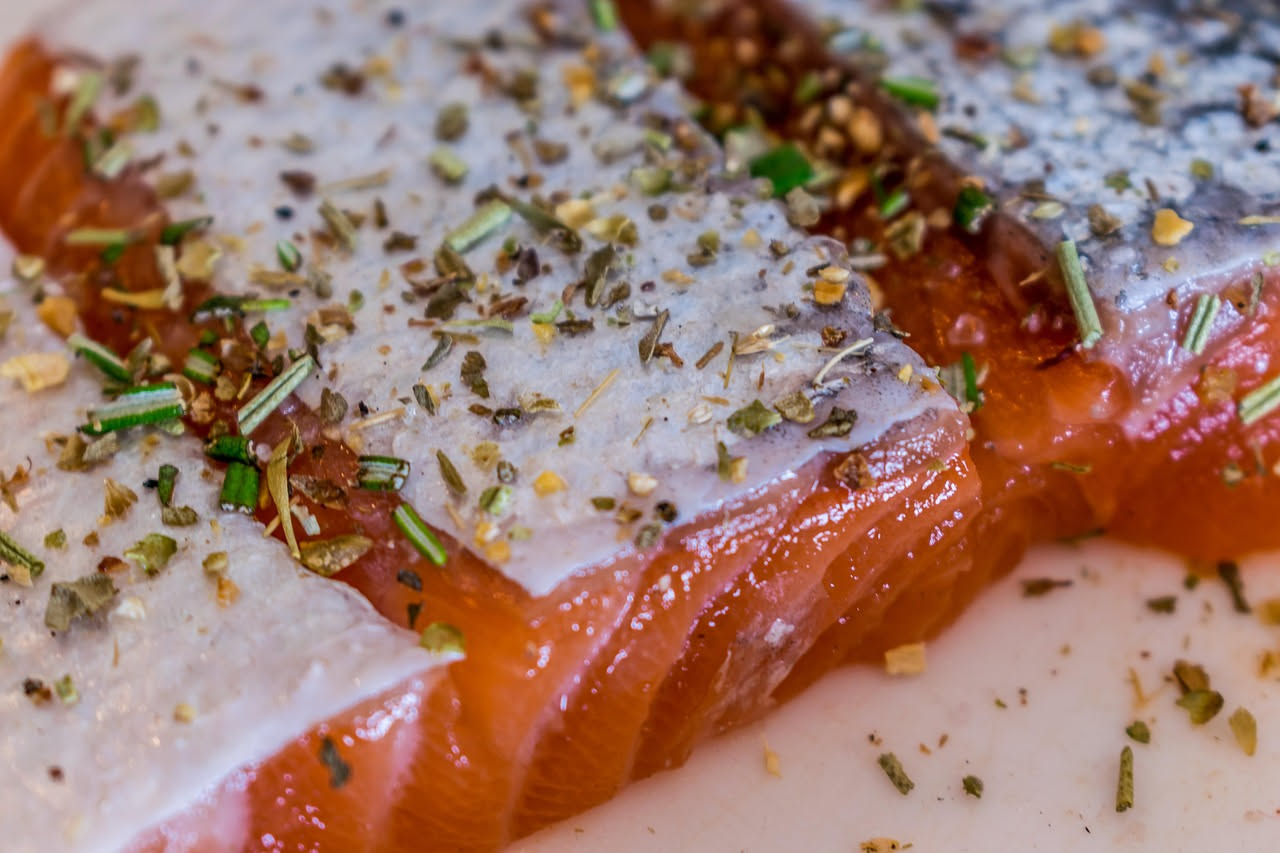 Due triglie intere dorate e croccanti in padella, con grani di sale marino visibili sulla pelle, contorno di limone fresco e prezzemolo sminuzzato, vapore che sale dal pesce appena cotto