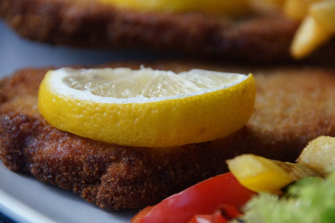 Trippa fritta dorata disposta su piatto bianco con contorno di limone fresco e prezzemolo verde, croccante in superficie, servita tiepida
