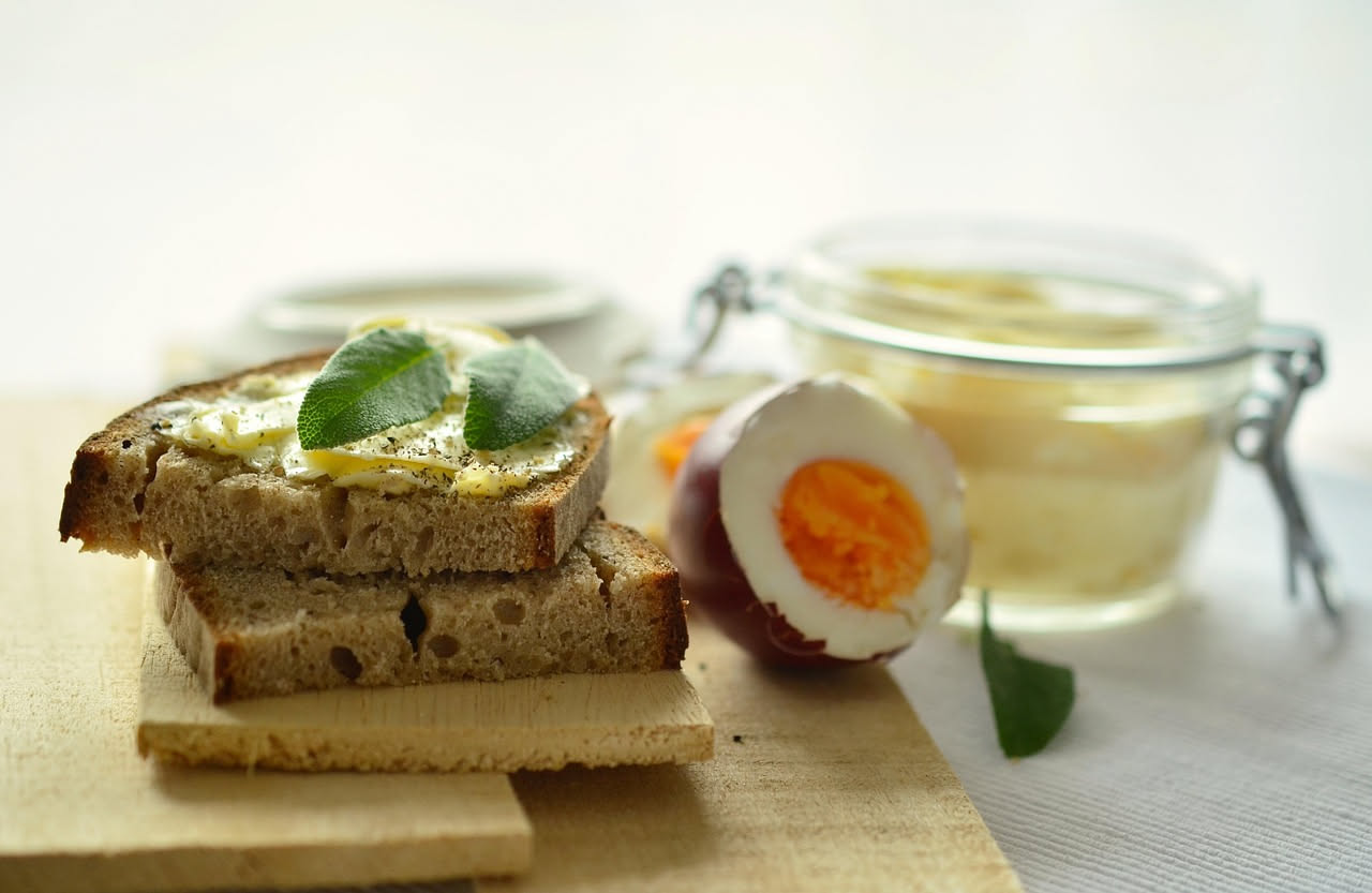 Due uova sode tagliate a metà su un piatto bianco, condite con maionese cremosa e una spolverata di pepe nero, accompagnate da fettine di pane tostato