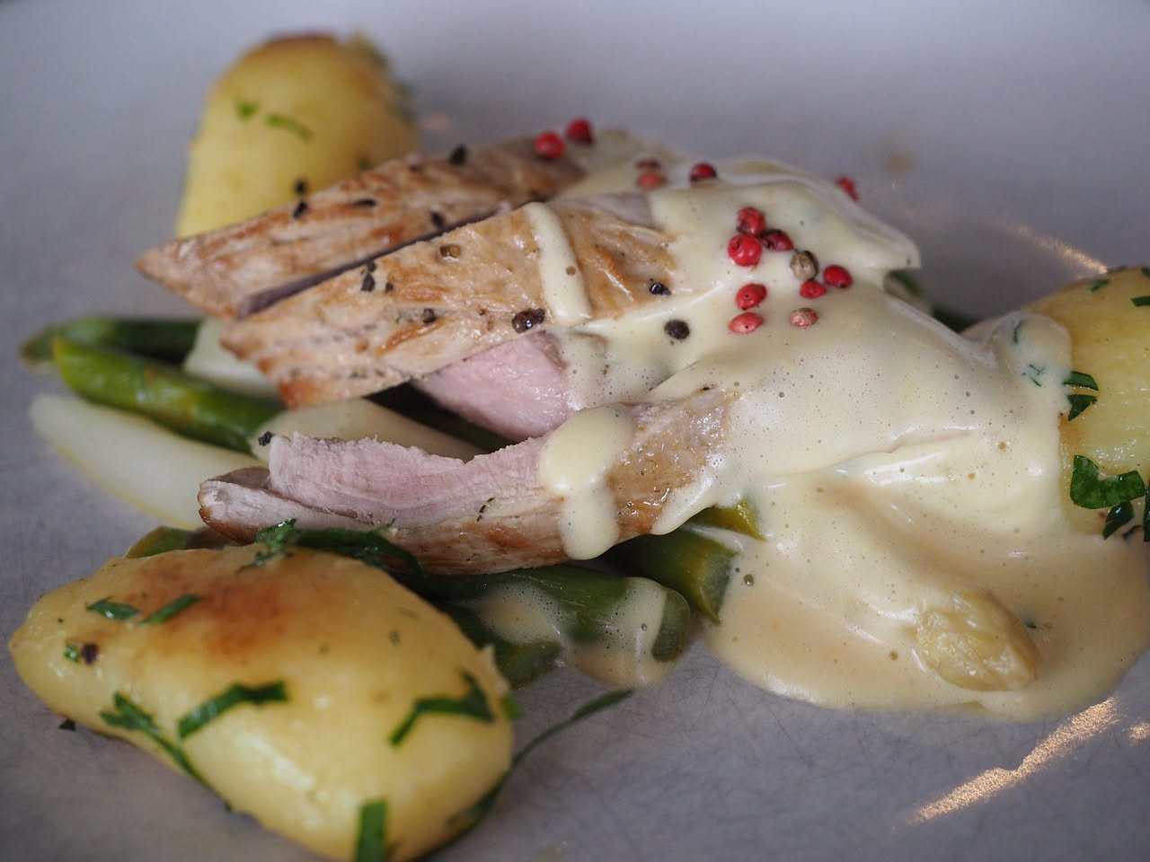 Vitello tonnato su piatto bianco: fettine di carne lessa rosate coperte da salsa beige cremosa, guarnite con filetti di acciuga e capperi verdi