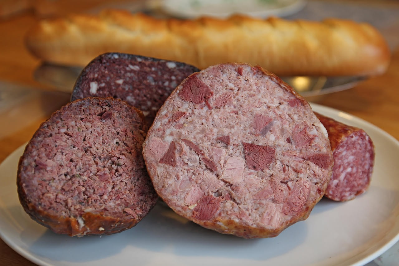Zampone affettato su piatto bianco con lenticchie marroni, accanto una posata d'argento e una candela accesa sullo sfondo