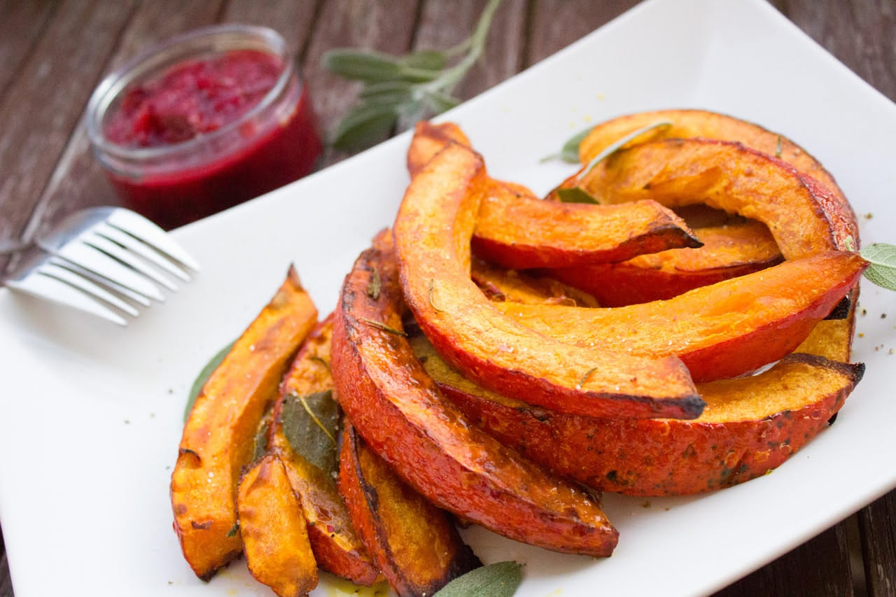Fette di zucca gialla fritte, dorate e croccanti, disposte su un piatto bianco con carta assorbente, cosparse di sale grosso