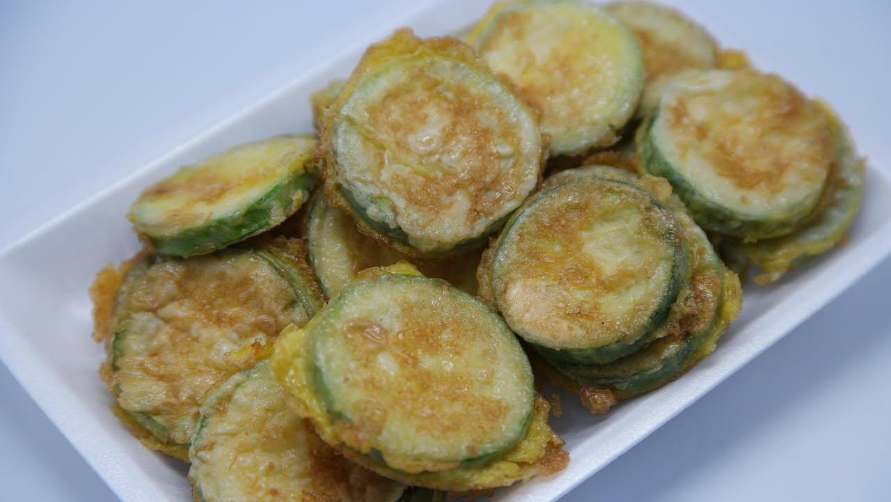 Zucchine trifolate fredde in ciotola bianca con fettine sottili di zucchina verde, aglio biancheggiante e prezzemolo fresco verde, su tavolo di legno chiaro