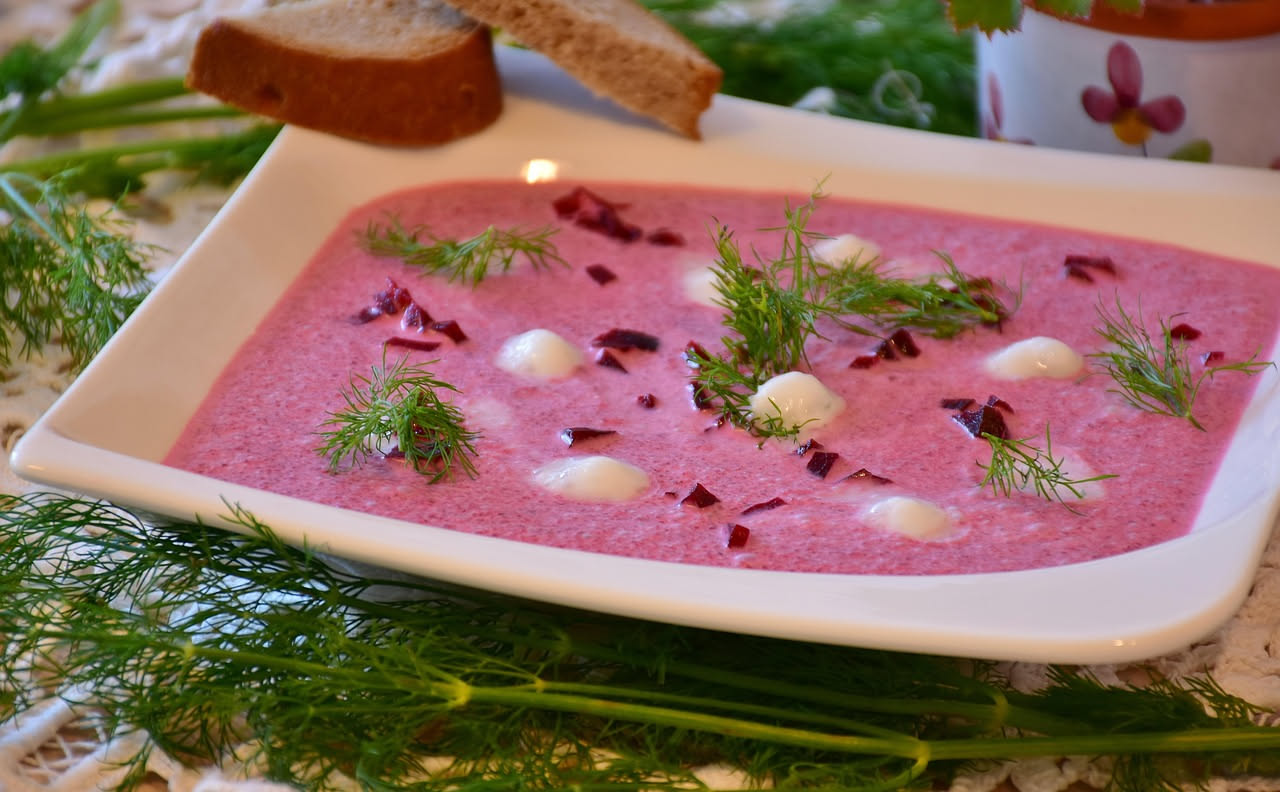 Una ciotola bianca riempita di zuppa d'avena cremosa di colore beige dorato, con verdure tagliate a dadini in superficie, qualche filo d'avena integrale visibile, accompagnata da un cucchiaio e da una