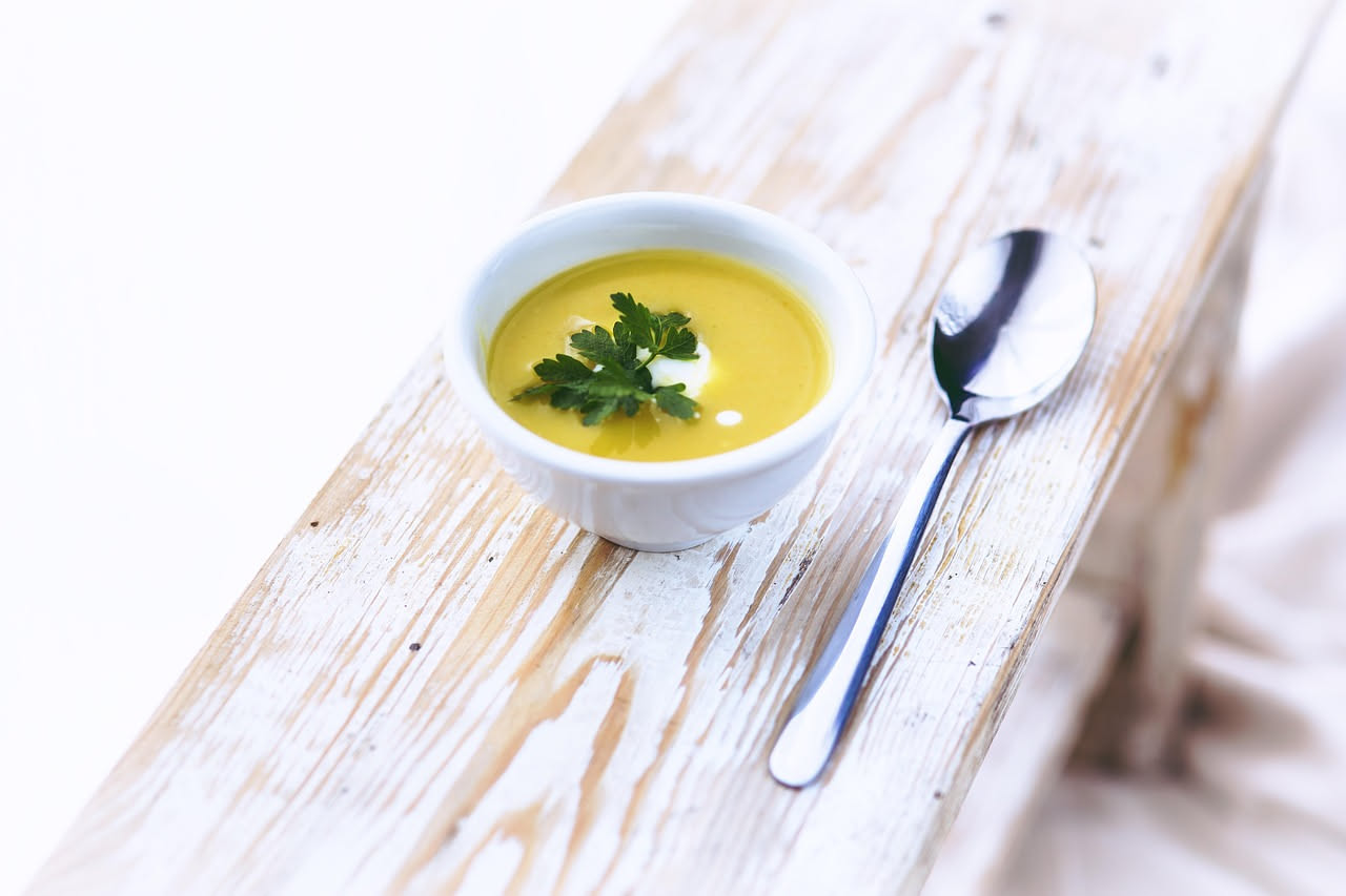 Zuppa d'orzo e cavoli in una ciotola di ceramica bianca, con pezzi visibili di cavolo verde, chicchi di orzo perlato e brodo trasparente leggermente dorato, guarnita da un filo d'olio d'oliva, su sfon