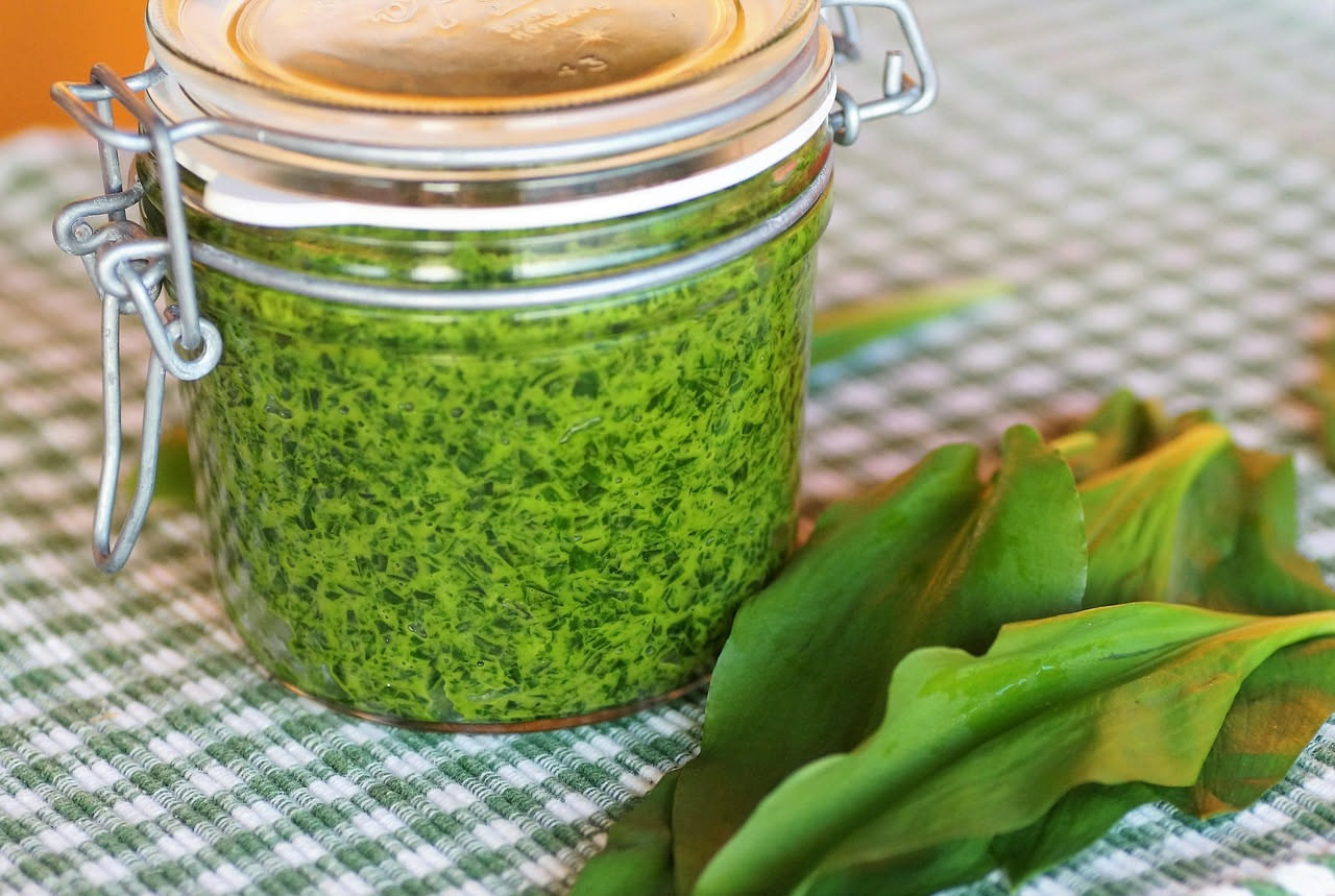 Zuppa di borragine di colore verde salvia in una ciotola bianca, liscia e cremosa, con un filo di olio di oliva in superficie, vapore leggero, cucchiaio di metallo sul bordo