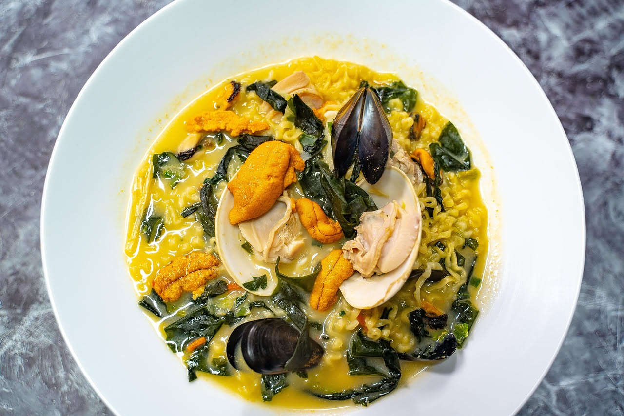 Zuppa di datteri di mare servita in ciotola bianca con brodo rosso-arancio, molluschi aperti color marrone scuro, crostini di pane tostato dorato ai bordi, prezzemolo fresco verde sparso in superficie
