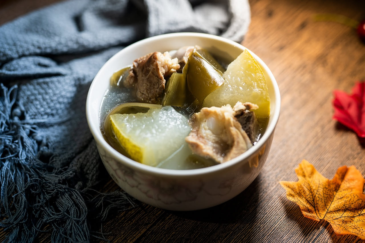 Zuppa di osso in ciotola di ceramica bianca, brodo dorato e traslucido con piccoli frammenti di verdure, guarnita con prezzemolo fresco su tavolo di legno