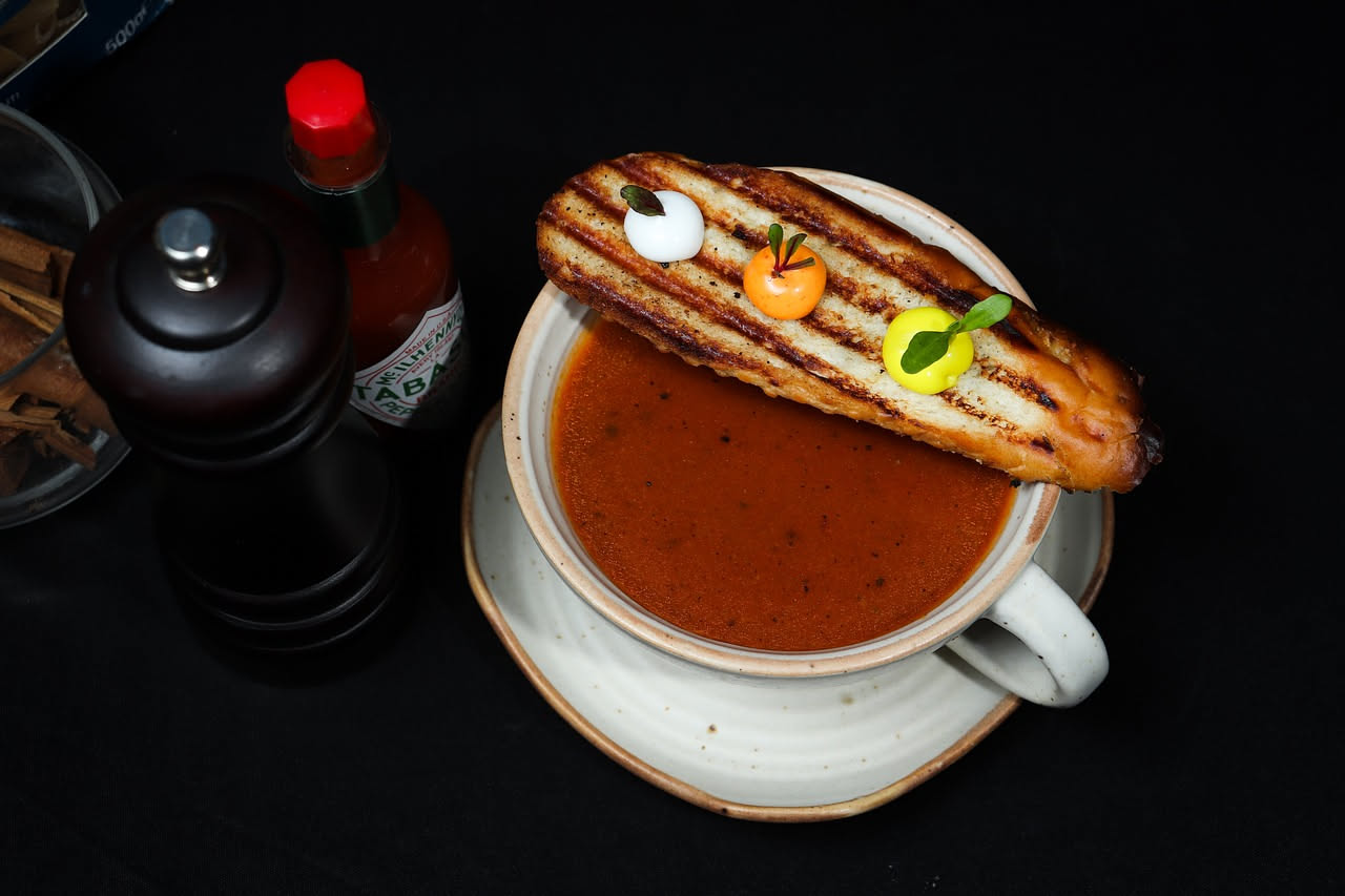 Zuppa di pane e pomodoro in una ciotola bianca, con pezzi di pane tostato ammorbiditi nel brodo rosso di pomodoro, foglia di basilico fresco, filo di olio d'oliva dorato in superficie, servita su tavo