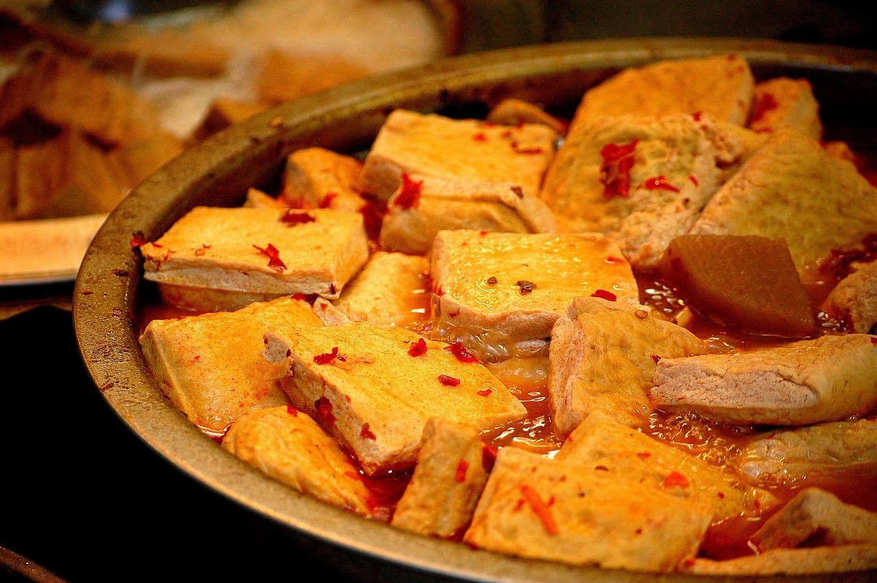 Una ciotola bianca con zuppa densa color avorio e marrone, garniture di farina di ceci fritta, gocce d'olio verde oliva in superficie, su sfondo di legno naturale