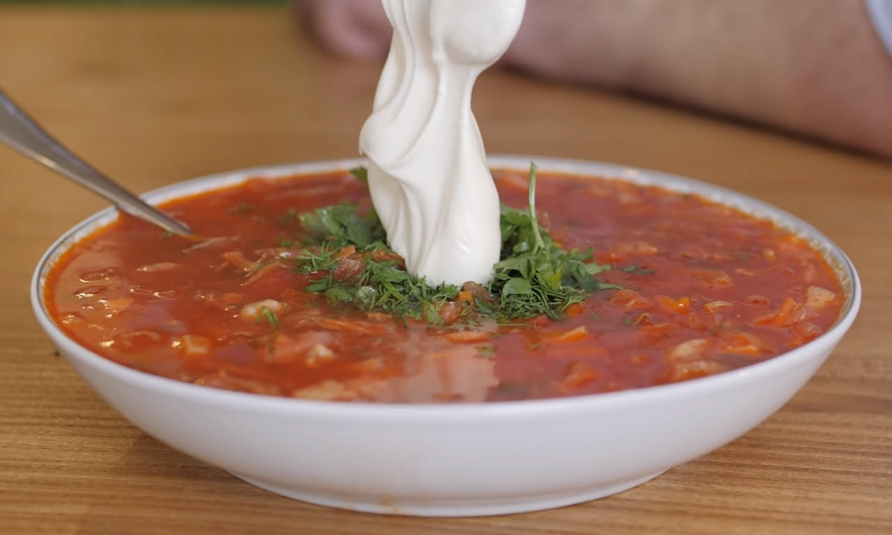 Zuppa di trippa in una ciotola bianca fonda, il brodo trasparente color ambra con strisce sottili di trippa cotta, cipolle dorate e sedano, con una spruzzata di prezzemolo fresco verde scuro in superf