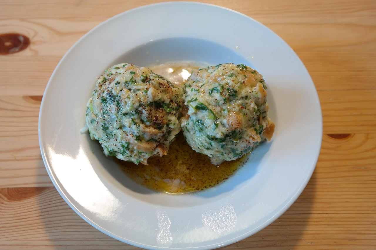 Ciotola di ceramica bianca con zuppa densa: brodo trasparente color ambra, cubetti di pane dorato ammorbidito, pezzetti di carota arancione e sedano, cipolla bianca, superficie liscia, cucchiaio di le
