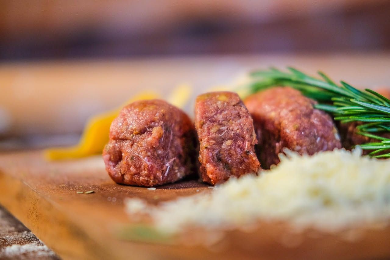Cotechino affettato in piatto bianco, in primo piano il colore rosa della carne e il grasso bianco, accompagnato da lenticchie scure e una forchetta
